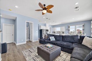 A spacious living room with a grey sectional sofa, a matching ottoman, and a ceiling fan. - Beachfront Luxury! New Build 2026! Hot Tub. Pets! (Surfside Beach)