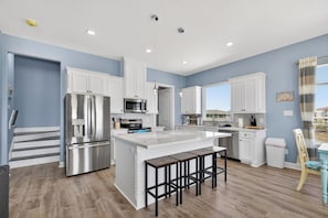 A modern kitchen with white cabinetry, stainless steel appliances, and a central island with bar stools.