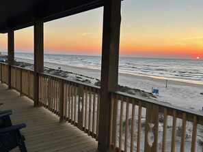 A wooden deck with a view of the beach and ocean during sunset.