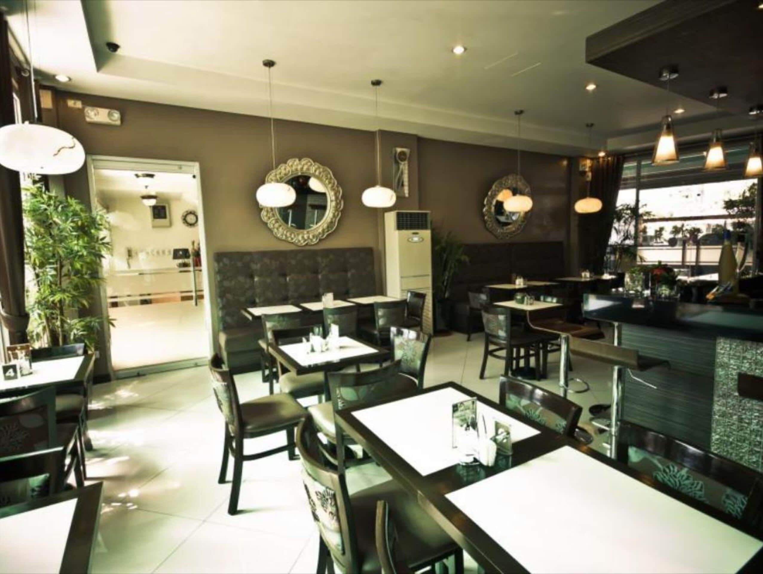L’intérieur d’un restaurant, avec de nombreuses tables et chaises, des luminaires suspendus et des miroirs décoratifs sur les murs.