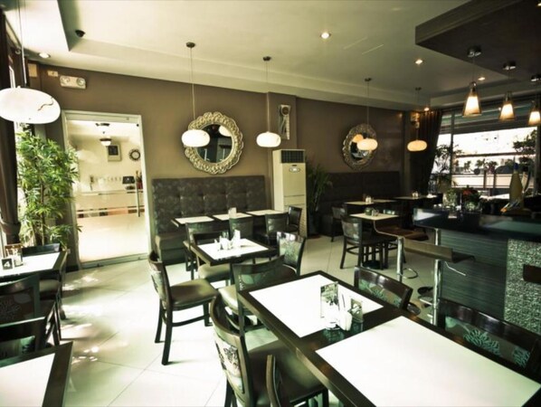 A restaurant interior with multiple tables and chairs, pendant lighting, and decorative mirrors on the walls.
