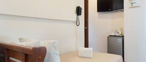 Habitación de hotel con cama de madera, ropa de cama blanca, un refrigerador pequeño, teléfono y televisor montado.