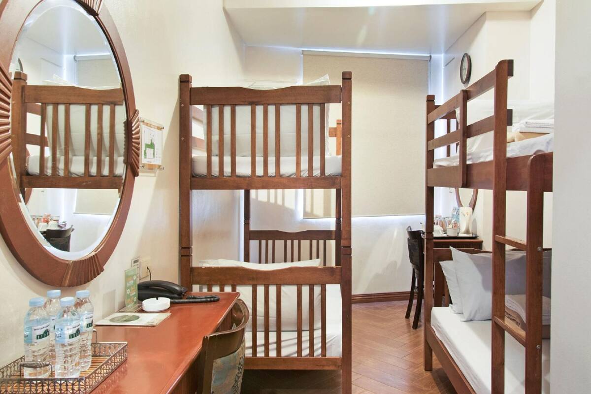 A compact room with bunk beds, a desk with a mirror, and a small table with water bottles.