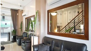 A modern hotel lobby with a leather sofa, a coffee table, and a large mirror reflecting the staircase and a dining area. - Townhouse OAK Metro Manila Near Osmena Highway PNR Pasay formerly Avitel Hotel (Makati)