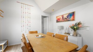 Un comedor con una mesa de madera, sillas, un adorno colgante, un cuadro y una planta en la pared.