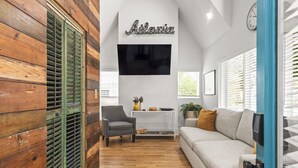 A modern living room with a grey sofa, a wooden accent wall, a mounted TV, and a small table with decorative items. - Hot Tub|Sauna|Walkable|Reynoldstown Spa Retreat (Atlanta)