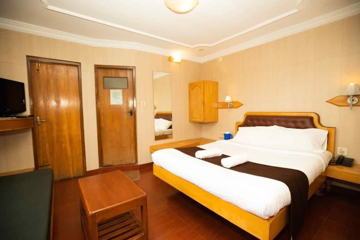 Ein Hotelzimmer mit einem hölzernen Bett, einem Nachttisch, einem Stuhl, einem Fernseher und einem Kleiderschrank.