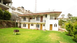 A two-story building with a balcony on the upper floor, a small lawn in front, and a stone wall to the left. - Lazo Silver Lake (Ootacamund)