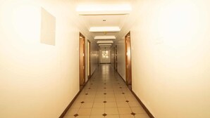 A long, narrow hotel corridor with doors on both sides, fluorescent lighting, and a tiled floor. - Lazo Silver Lake (Ootacamund)