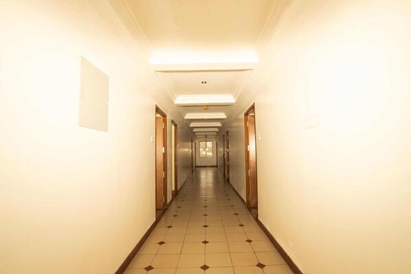 A long, narrow hotel corridor with doors on both sides, fluorescent lighting, and a tiled floor. - Lazo Silver Lake (Ootacamund)