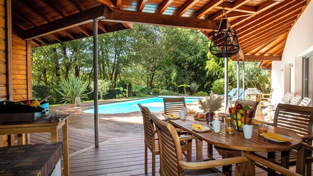 Une terrasse en bois avec une piscine, entourée d’une végétation luxuriante.