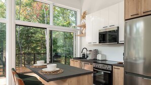 A modern kitchen with a large island, stainless steel appliances, and a view of a forest through large windows.