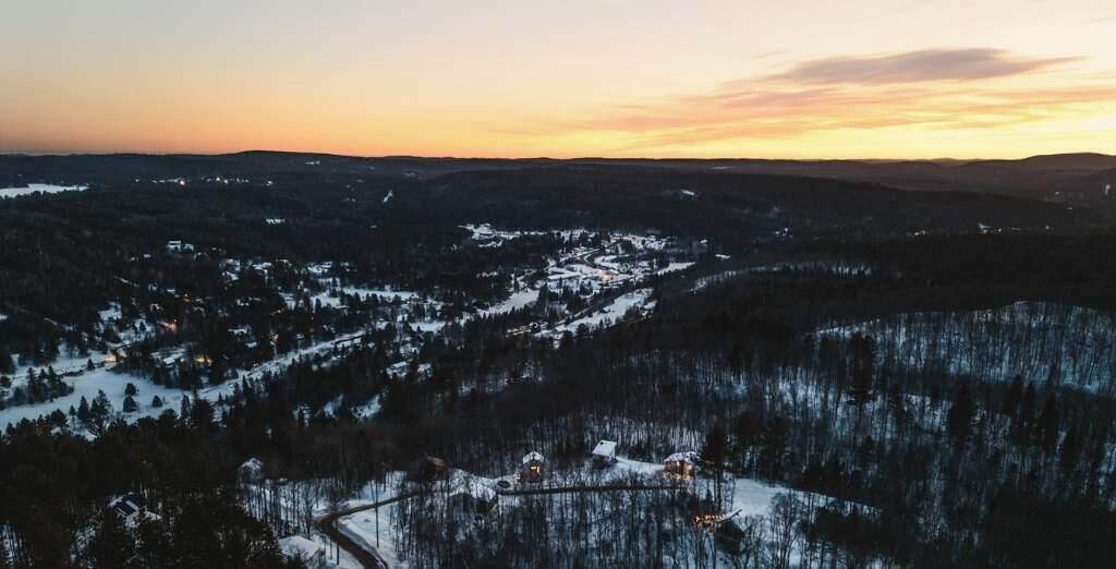 A panoramic view of a snow-covered landscape with a small settlement and forested hills.