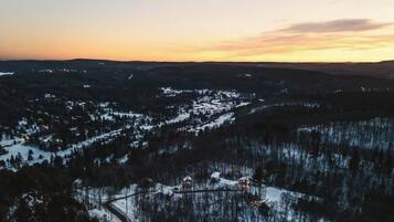 Une vue panoramique d’un paysage enneigé, avec un petit village et des collines boisées.