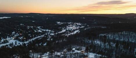 A panoramic view of a snow-covered landscape with a small settlement and forested hills.