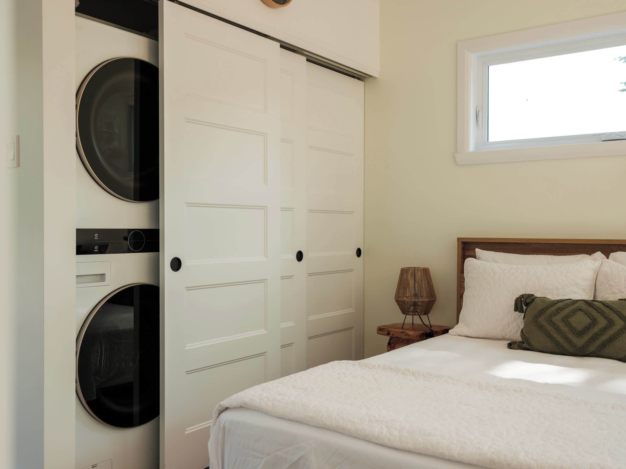A bedroom with a bed, a window, a lamp, and a washing machine.
