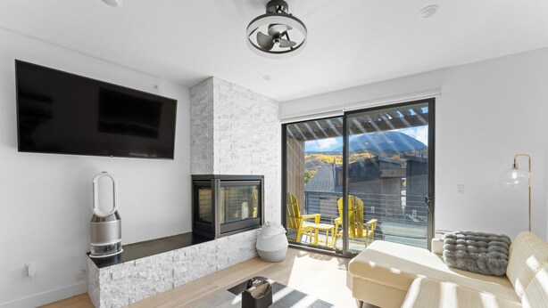 Ein modernes Wohnzimmer mit Flachbildfernseher, Kamin, Sofa und einer großen Glastür zum Balkon.
