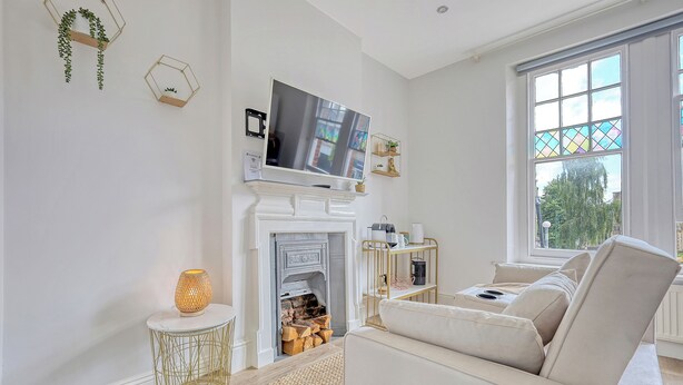 A modern living room with a white fireplace, a flat-screen TV, and a beige sofa. - Wanstead Gem – Bright, Cosy & Immaculate High Street Apartment in East London (London)