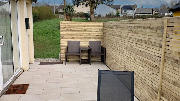 A patio with two wicker chairs and a table, a wooden fence, and a grassy area with trees. - Seamount Holiday Village No 26 (Courtown)