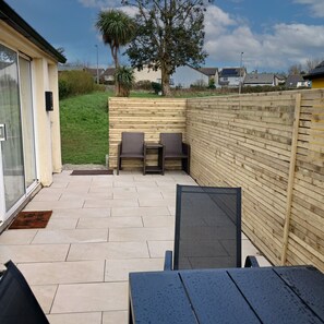 A patio with two wicker chairs and a table, a wooden fence, and a grassy area with trees. - Seamount Holiday Village No 26 (Courtown)