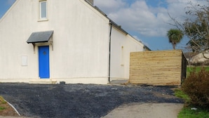 A white building with a blue door, a chimney, and a small window. - Seamount Holiday Village No 26 (Courtown)