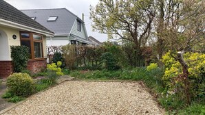 Un immobile residenziale con vialetto sterrato, una casa con tetto spiovente e un giardino con diverse piante e alberi.