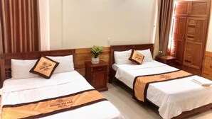 Een hotelkamer met twee bedden, houten hoofdborden, een klein nachtkastje met een plantje en een kledingkast.