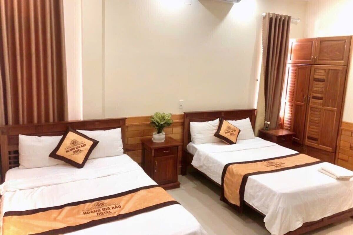 A hotel room with two beds, wooden headboards, a small bedside table with a plant, and a wardrobe.