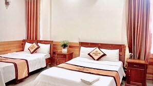 Een hotelkamer met twee enkele bedden, houten hoofdborden, een klein nachtkastje met een plant erop, en een wandairconditioner.