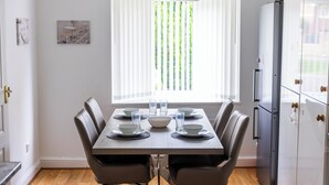 A dining area with a table set for six, a refrigerator, and a window with blinds. - A Stunning Four Bed House in Posh Oadby, Leicester (Leicester)