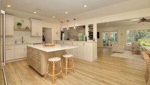 Una cocina amplia con una isla grande, armarios blancos y piso de madera.