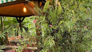 A covered outdoor seating area with a bench and a table, surrounded by lush greenery and various plants. - Bungalow Le Refuge Vert (Morne-à-l'Eau)