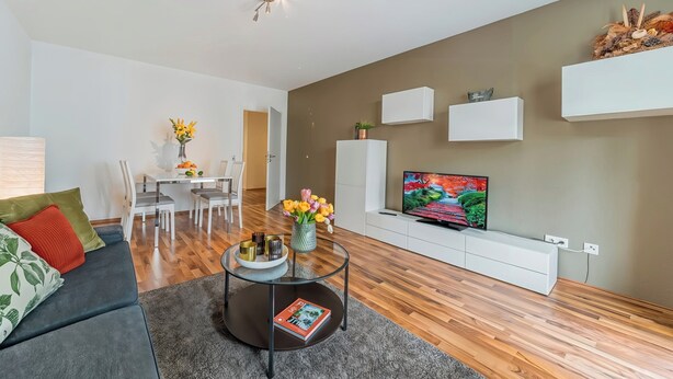 A modern living room with a sofa, coffee table, TV, and a dining area with chairs and a table. - Cozy Stylish Berlin Apartment With 2 Bedrooms (Berlin)