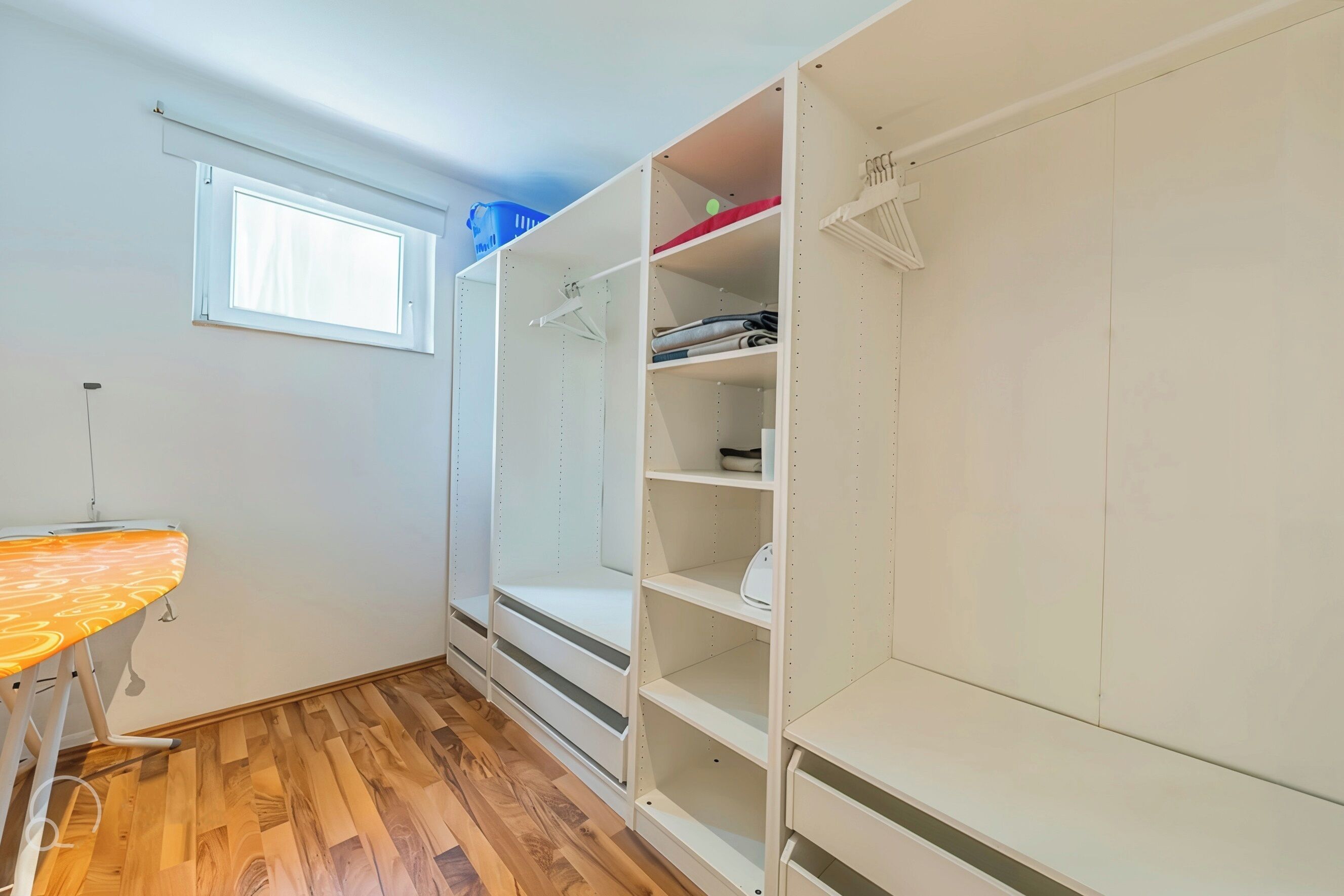 A room with a wooden floor, a window, and a white closet with shelves and hanging space.