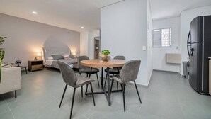 A modern living space with a round dining table, grey chairs, a bed with a grey headboard, a black refrigerator, and a small plant on the table. - Luxury Studio - Tesoro, Provenza, and Parque Lleras (Medellín)