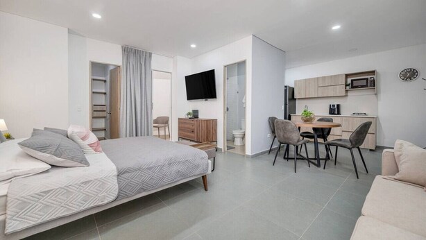 A modern, well-lit bedroom with a large bed, a desk, and a kitchenette. - Luxury Studio - Tesoro, Provenza, and Parque Lleras (Medellín)