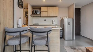 A modern kitchen with wooden cabinets, a stainless steel refrigerator, and two grey bar stools. - 7th floor modern apartment close to parque lleras (Medellín)