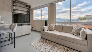 A modern living room with a sofa, a TV, and a dining area with a chair.