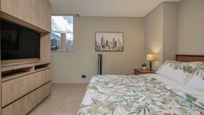 Une chambre d’hôtel avec un lit, une télévision, un tableau représentant un paysage urbain et une fenêtre donnant sur des immeubles.