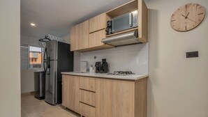 Una cocina compacta con armarios de madera, un refrigerador de acero inoxidable, un microondas y un reloj en la pared.