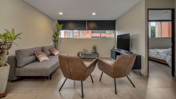 Una sala de estar moderna con un sofá gris, dos sillones marrones, un televisor y una mesita con una planta.