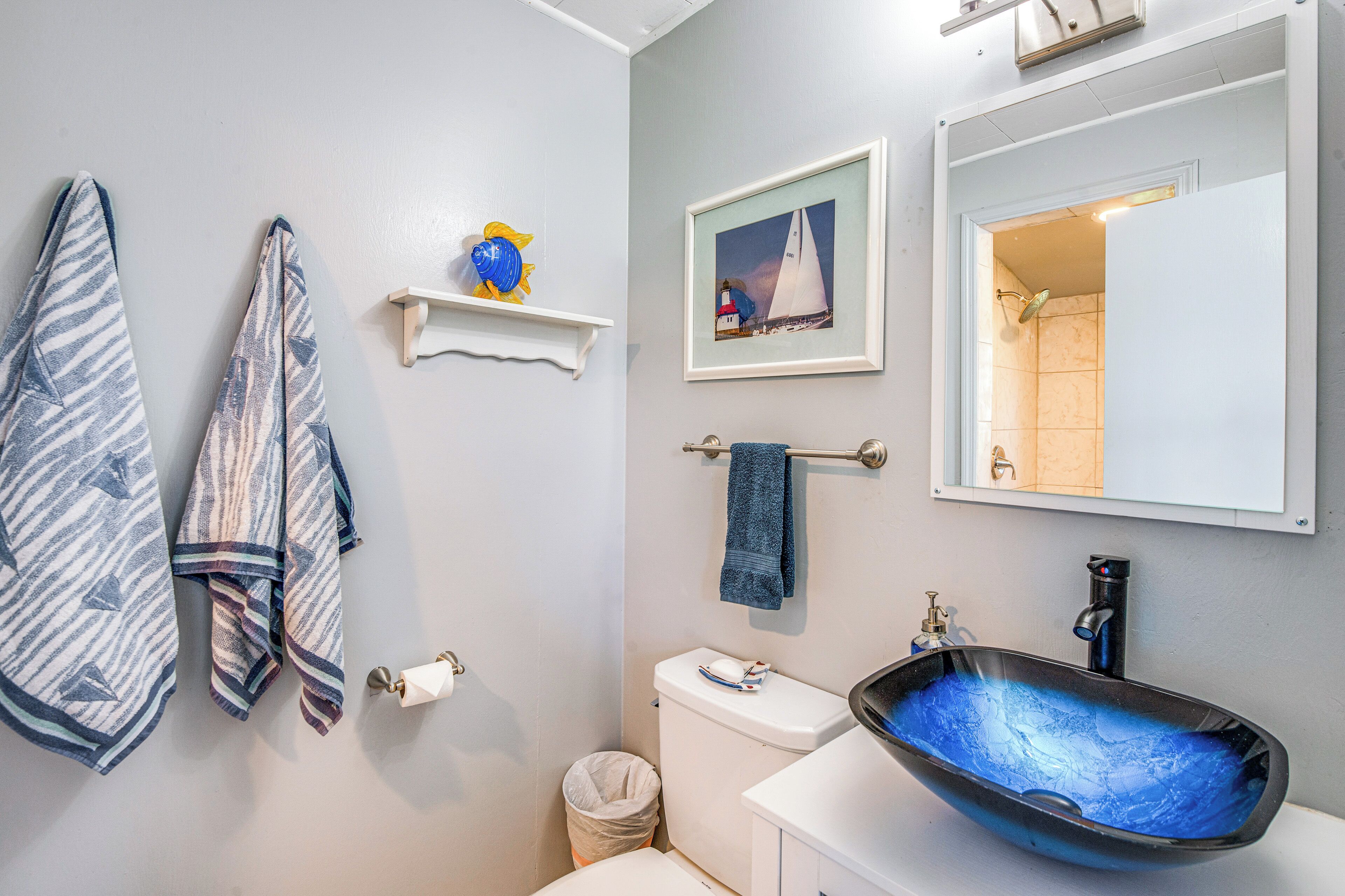 Une salle de bain avec un lavabo blanc, un tableau encadré représentant un voilier, un porte-serviettes et des toilettes.