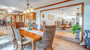 Un'ampia sala da pranzo con un tavolo in legno e sedie in vimini, una cucina sullo sfondo e un cartello con la scritta "The Garden House".