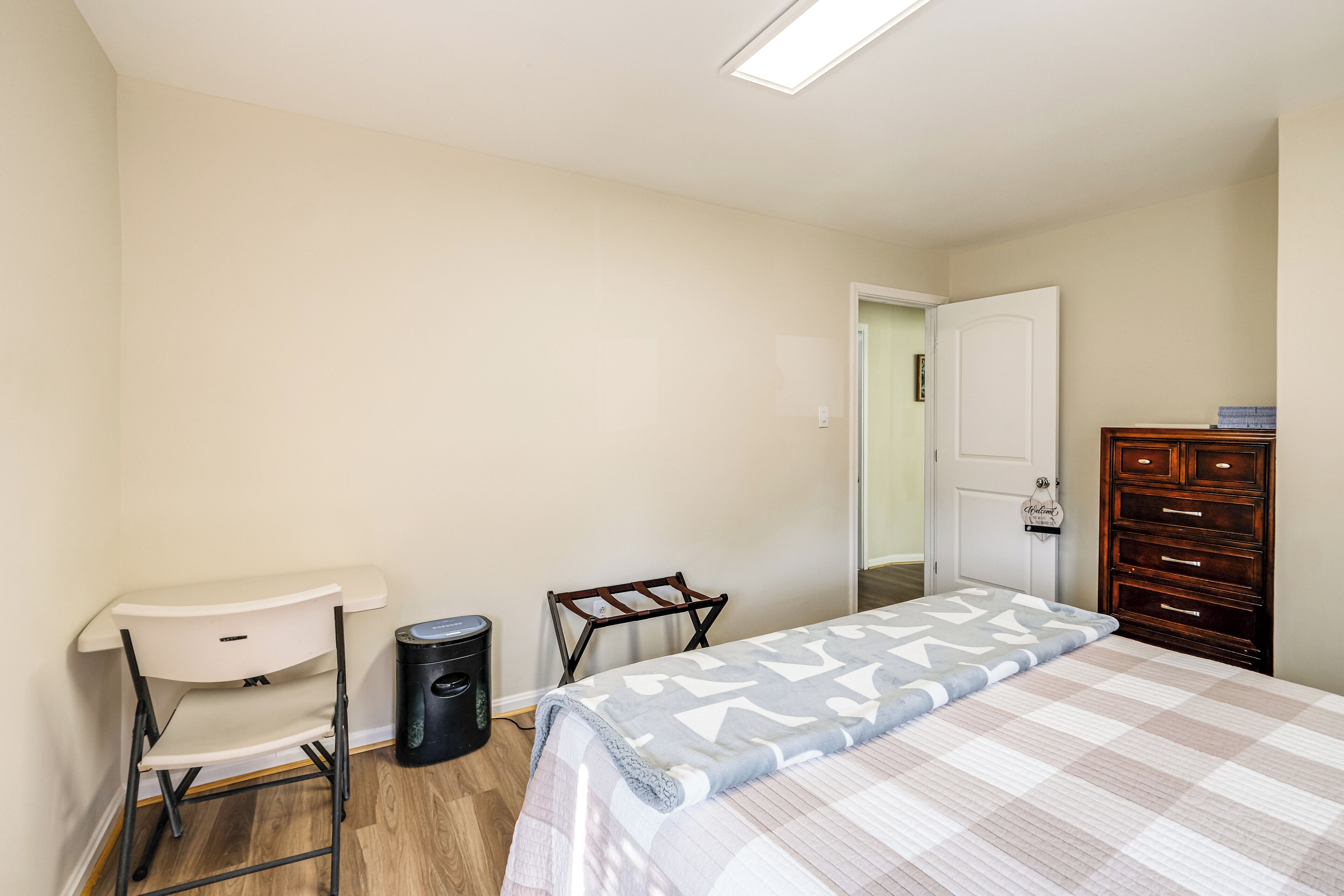 A bedroom with a bed, a desk, a chair, a dresser, and a door.