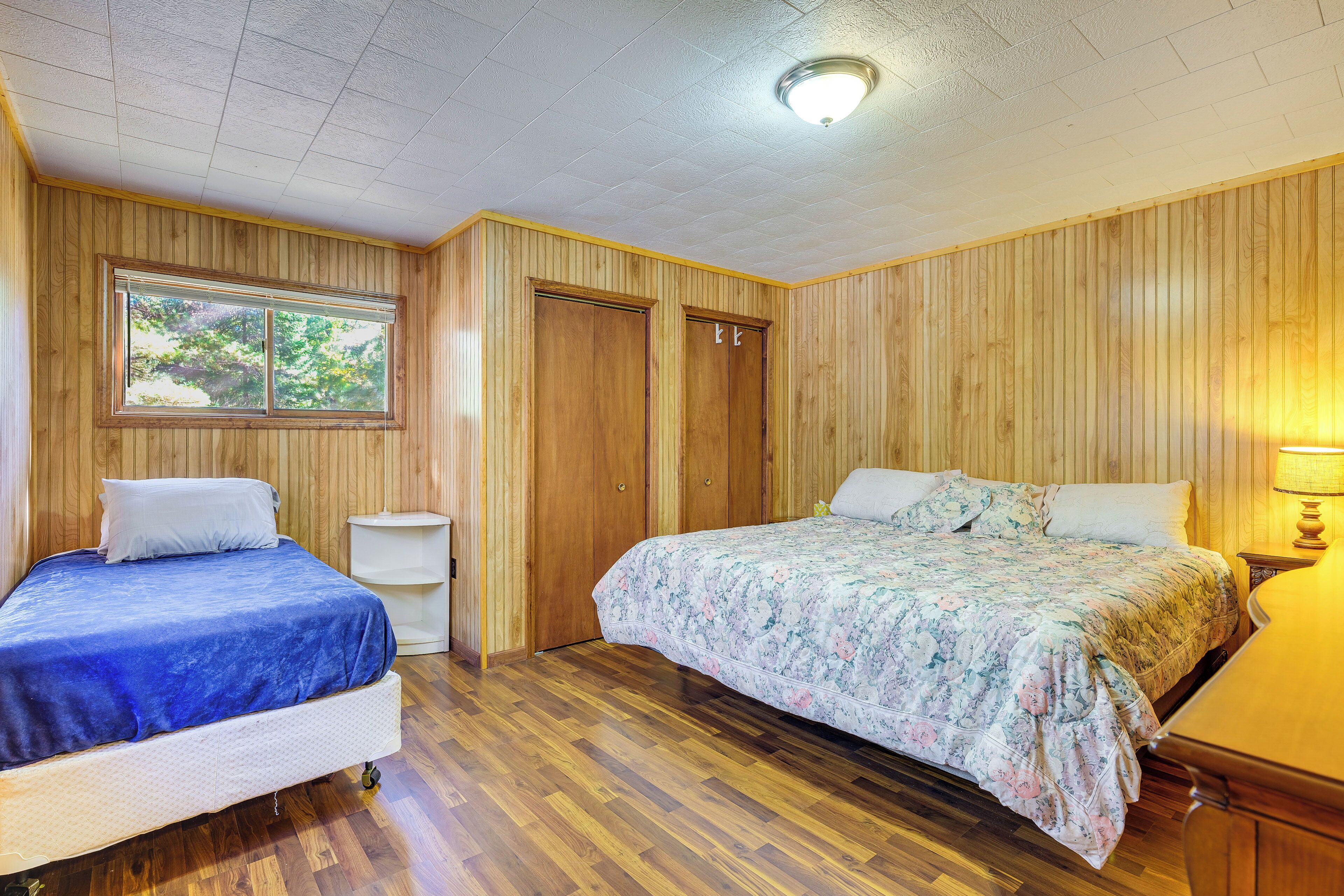Un dormitorio con dos camas, paredes de madera, una ventana y una lámpara en el techo.