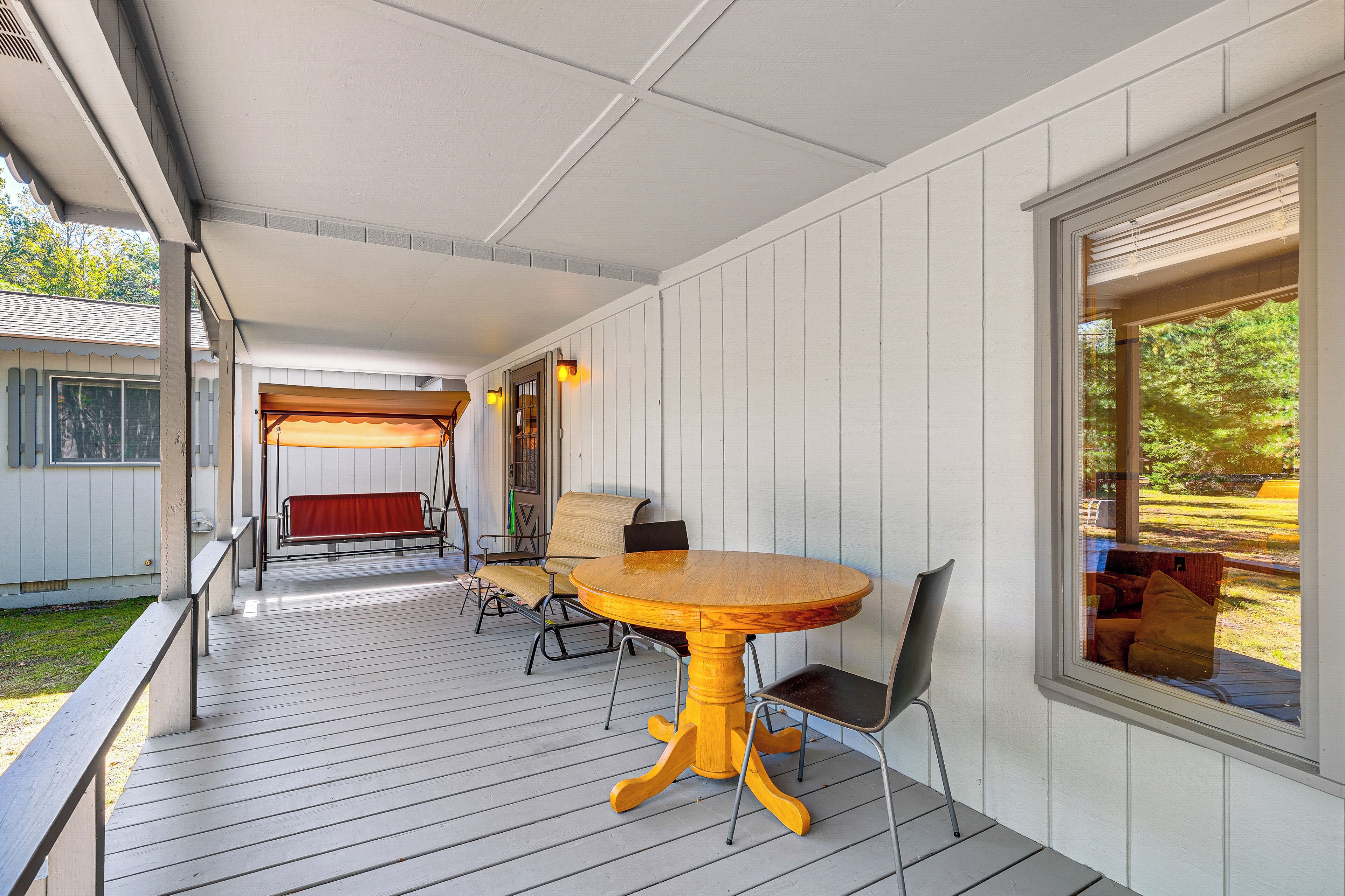A covered outdoor area with a wooden table and chairs, a swing, and a view of the outdoors.