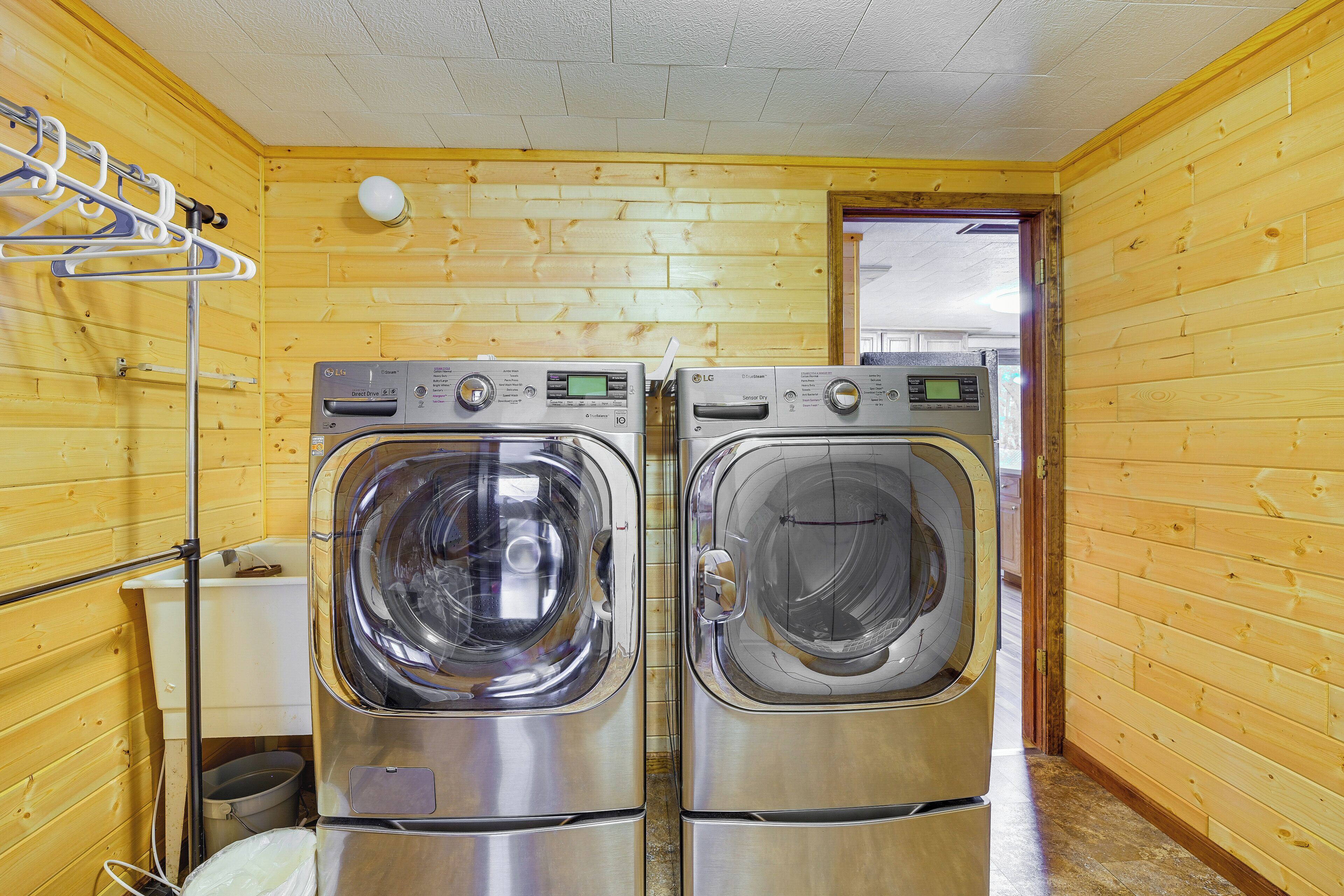 A laundry room with two stainless steel front-loading washers and dryers, wooden walls, and a metal drying rack.