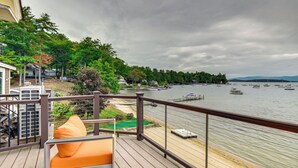 A wooden deck with a view of a lake, boats, and a forested area. - Lake Winnipesaukee Condo w/ Beach Access! (Gilford)