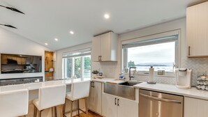 A modern kitchen with white cabinetry, stainless steel appliances, and a large window offering a view of the sea. - Lake Winnipesaukee Condo w/ Beach Access! (Gilford)
