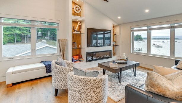 A spacious living room with a fireplace, large windows with a view of boats, and a cozy seating area. - Lake Winnipesaukee Condo w/ Beach Access! (Gilford)